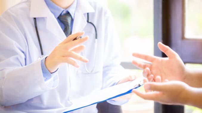 Doctor man consulting patient while filling up an application form at the desk in hospital.