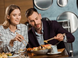 Happy young adult couple eating sushi rolls in restaurant