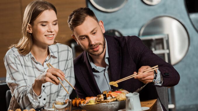 Happy young adult couple eating sushi rolls in restaurant