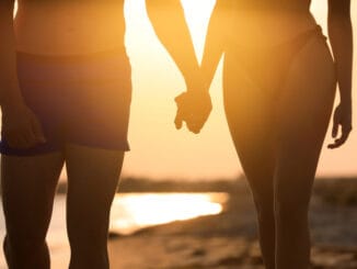 Woman in bikini holding hands with her boyfriend on beach at sunset