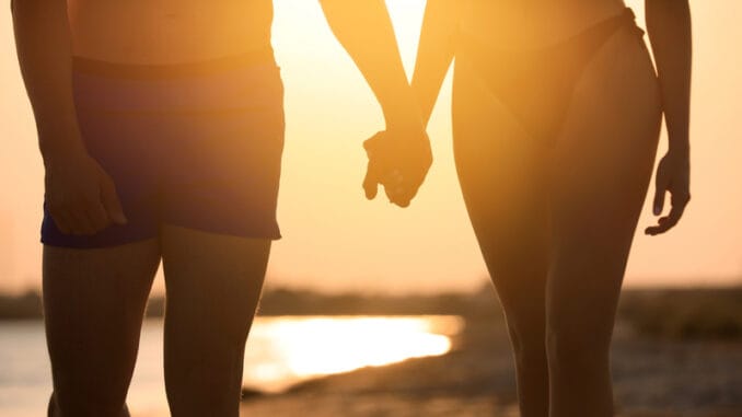 Woman in bikini holding hands with her boyfriend on beach at sunset
