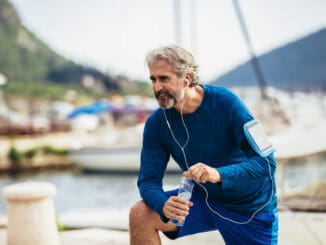 Fit thirsty senior man drinking water before running.