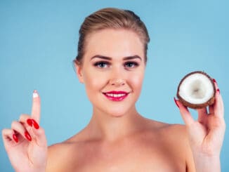 Beautiful woman with perfect skin make-up red lips holding coconut blue background in studio .spa and organic oil cosmetics idea.