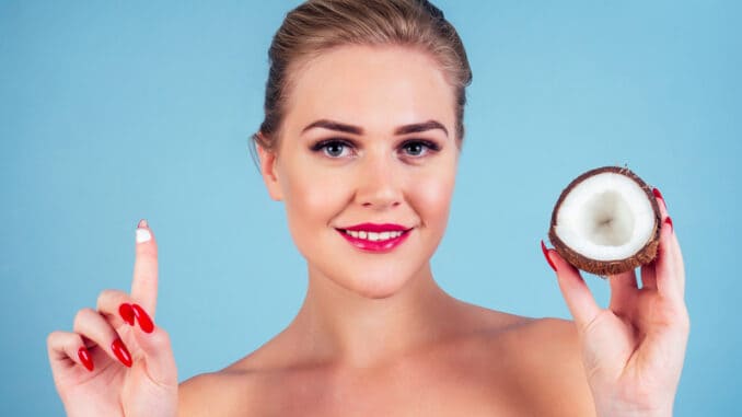 dreamstime_s_160103794 Beautiful woman with perfect skin make-up red lips holding coconut blue background in studio .spa and organic oil cosmetics idea.