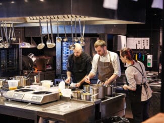 Three cooks in the kitchen prepare dishes using a variety of kitchen accessories