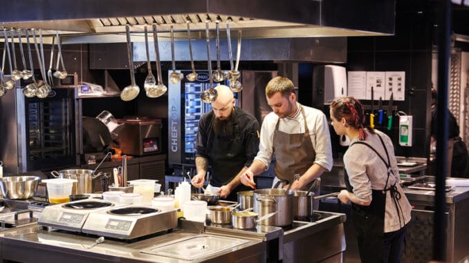 Three cooks in the kitchen prepare dishes using a variety of kitchen accessories