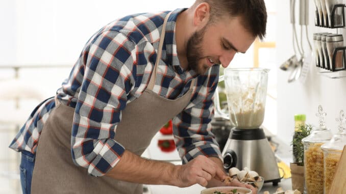 Young man cooking tasty cream soup with mushrooms