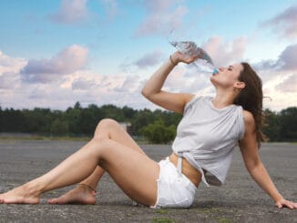 Young woman in shorts sitting on pavement and drinking wate