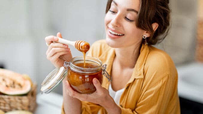 Portrait of a young and cheerful woman with a jar full of sweet honey on the kitchen at home