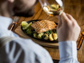 Young man eating salmon fillet with gratinated potatoes, leek and spinach in the restaurant with glass of white wine