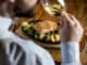 Young man eating salmon fillet with gratinated potatoes, leek and spinach in the restaurant with glass of white wine