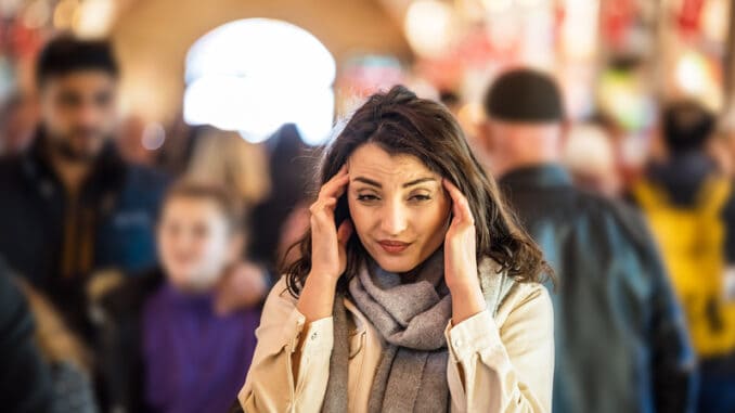 Beautiful woman in fashionable modern clothes suffers migraine or headache problem while standing crowd of people at road