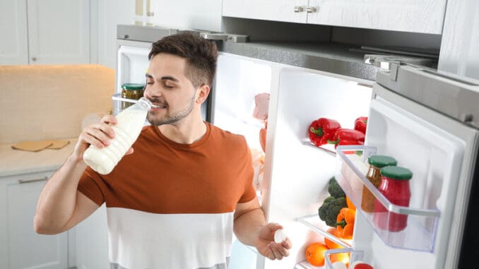 dreamstime_s_177726400 Young man drinking milk near open refrigerator in kitchen