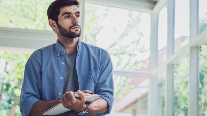 dreamstime_s_177903938 A man looking and thinking at note book while working at home office