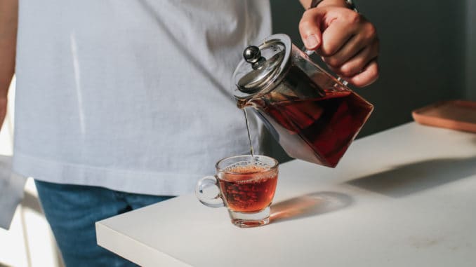 Close up man pouring hot tea from teapot into small glass near window.