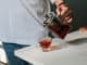 Close up man pouring hot tea from teapot into small glass near window.