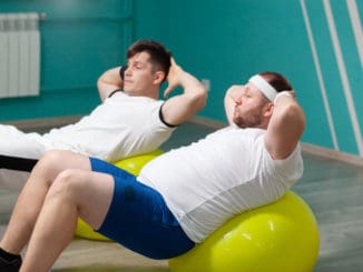 Tired fat man is lying on a fitness ball training during group fitness classes.