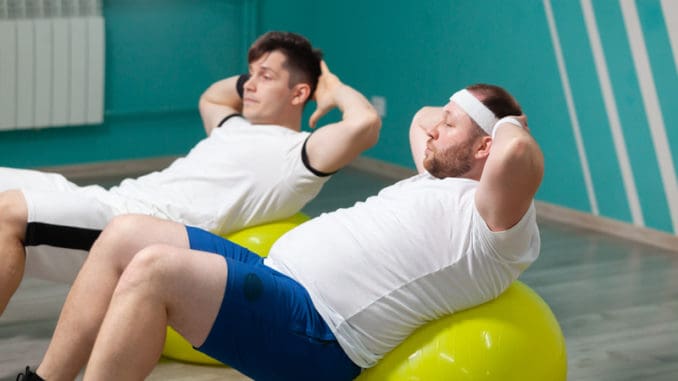 dreamstime_s_181848433 Tired fat man is lying on a fitness ball training during group fitness classes.