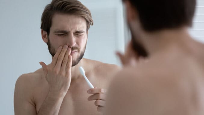 Young caucasian man wash brush teeth in bathroom have painful feeling suffer from gingivitis or periodontitis, millennial male struggle with oral dental problems, gums bleeding or inflammation