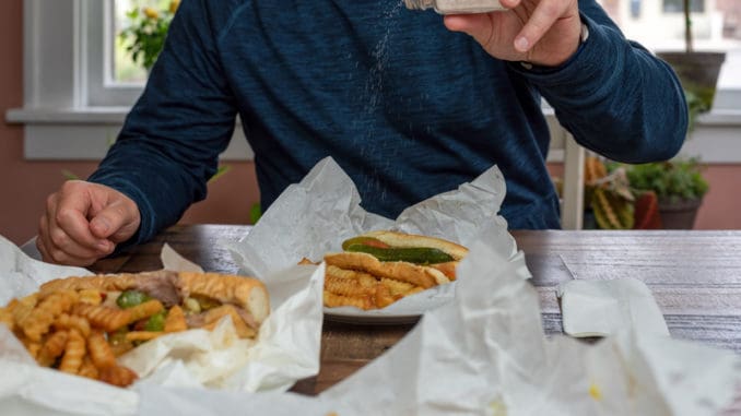 Supporting local restaurants by ordering takeout for lunch - a man is adding salt to his french fries