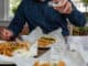 Supporting local restaurants by ordering takeout for lunch - a man is adding salt to his french fries