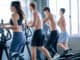 Beautiful sport women exercise with elliptical machine among the other men in the gym with day light.