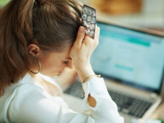 Seen from behind woman with empty blister pack of pills buying pharmacy on internet on a laptop in the living room
