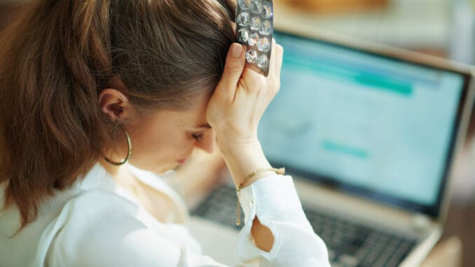 Seen from behind woman with empty blister pack of pills buying pharmacy on internet on a laptop in the living room