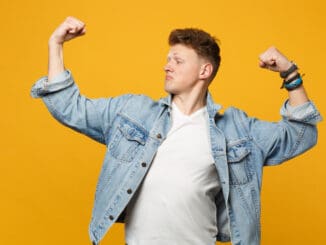 Portrait of strong young man in denim casual clothes looking aside, showing biceps,