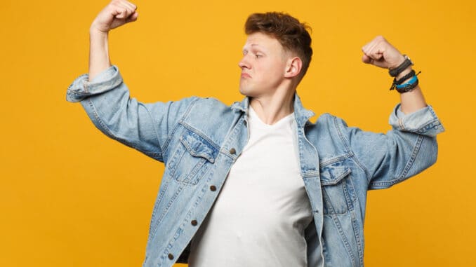 Portrait of strong young man in denim casual clothes looking aside, showing biceps,