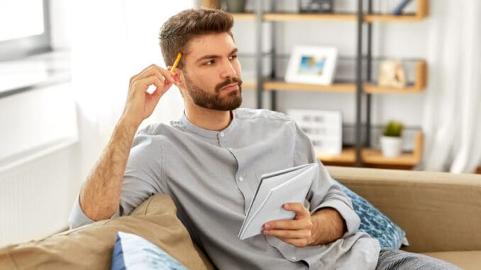 man writing to notebook and thinking at home