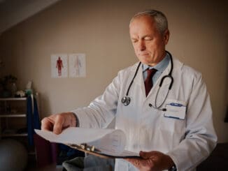 Senior male doctor holding clipboard checking reports in hospital