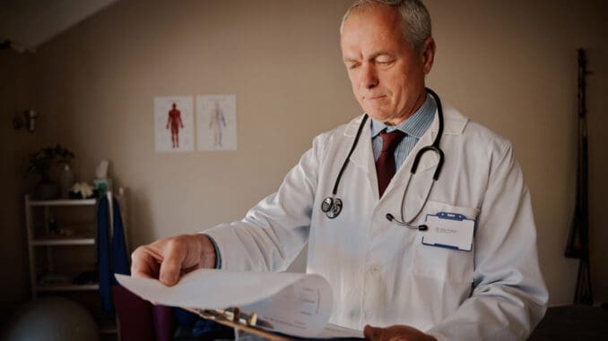 dreamstime_s_197062999 Senior male doctor holding clipboard checking reports in hospital