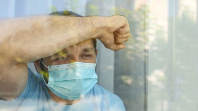 dreamstime_s_198261686 Stressed man in protective mask looking out of window