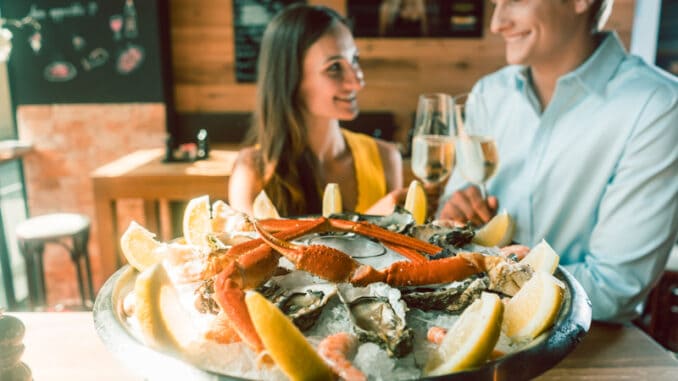 Close-up of fresh oysters and crabs served on ice with slices of lemon at the table of a romantic young couple eating at restaurant