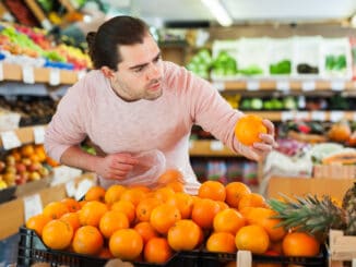 Young man customer looking fresh oranges in fruit store
