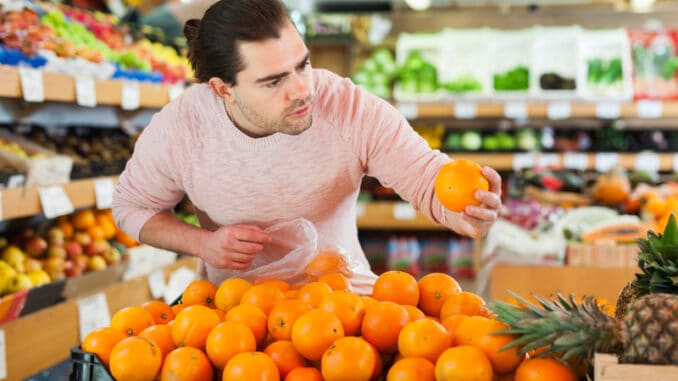 dreamstime_s_199354587 Young man customer looking fresh oranges in fruit store