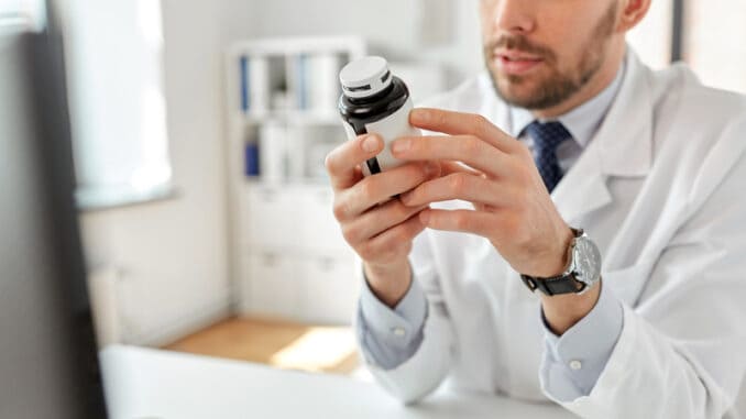 Healthcare, medicine and people concept - smiling male doctor with drug in jar at hospital