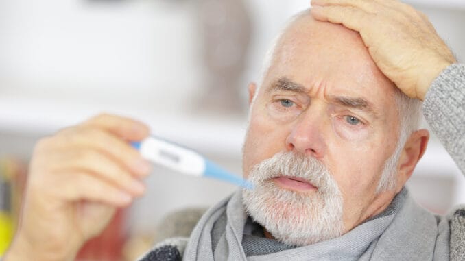 Senior man checking body temperature with thermometer