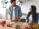 Smiling women and men cooking salad in the kitchen together.