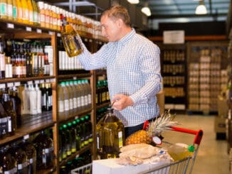 Portrait of glad cheerful positive man buying olive oil in supermarket