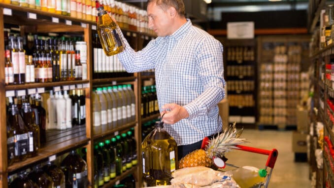 Portrait of glad cheerful positive man buying olive oil in supermarket