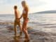 Romantic couple holding hands and wading in the sea shore in the evening.