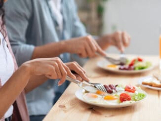 Unrecognizable couple using fork and knife while eating tasty breakfast in kitchen