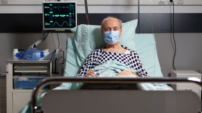 Portrait of sick senior man patient with chirurgical mask resting in hospital bed