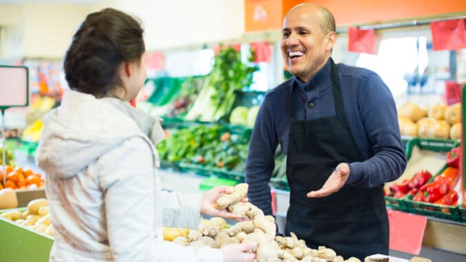 friendly salesman helping female customer to choose ginger in supermarket