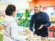 friendly salesman helping female customer to choose ginger in supermarket