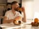 Young man eating croissant and drinking tea or coffee on breakfast