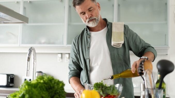 Mature man cooking vegetables salad in home kitchen.