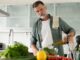 Mature man cooking vegetables salad in home kitchen.